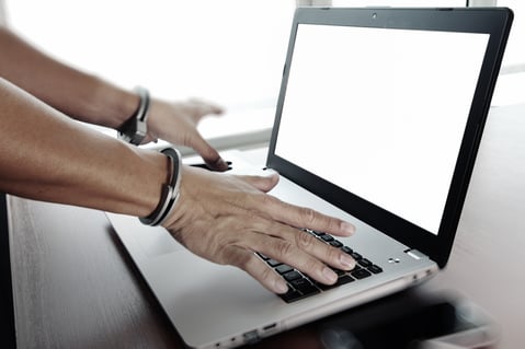 Businessman hand in handcuffs at wooden desk with laptop computer and digital tablet and stylus pen and smart phone as Cyber-Crime concept-1